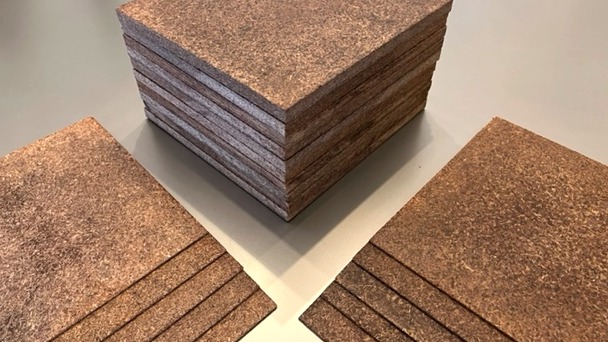 A stack of finished structural boards pressed from coconut biomass, with loose sheets fanned in front showing the cut edge.